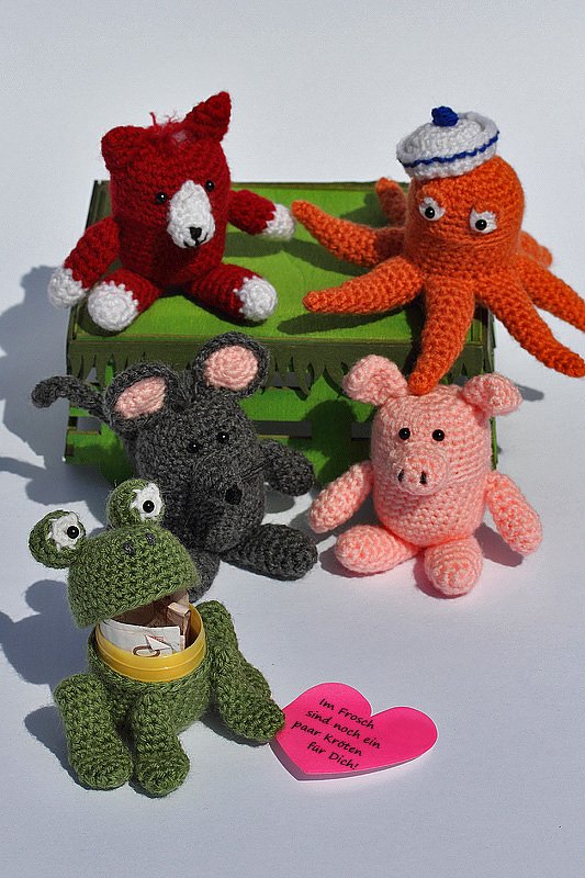 Gehäkelte Amigurumi-Tiere: rotes Tierchen, Oktopus mit Matrosenmütze, Maus, Schwein und ein grüner Frosch, der als Geldgeschenk mit Geldscheinen dient.
