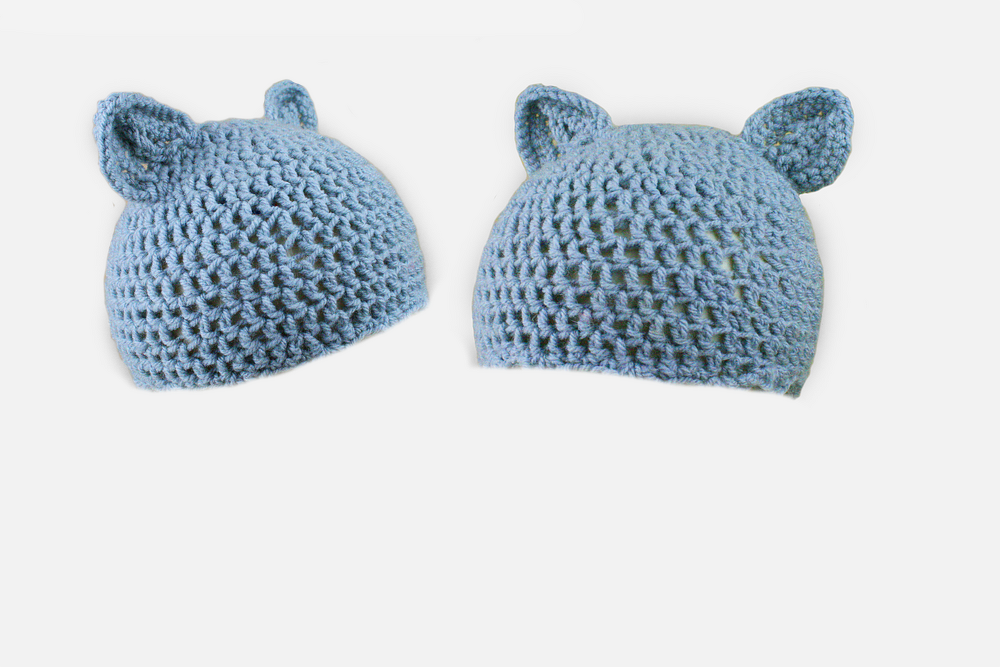 Zwei hellblaue gehäkelte Babymützen mit Ohren auf weißem Hintergrund