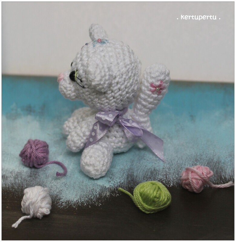 Weiße Amigurumi-Katze mit lila gepunkteter Schleife und Garnknäueln