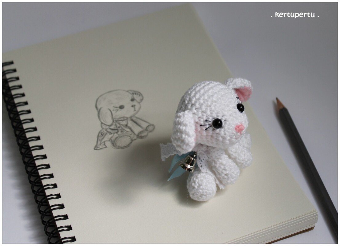 Weißes gehäkeltes Amigurumi-Hündchen mit Glocke auf Skizzenblock