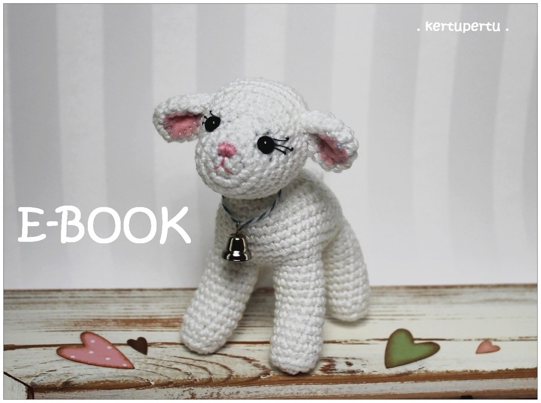 Vollansicht eines weißen gehäkelten Lämmchens mit kleiner Glocke um den Hals, auf einer Holzoberfläche; im linken Bereich des Bildes steht 'E-BOOK'.