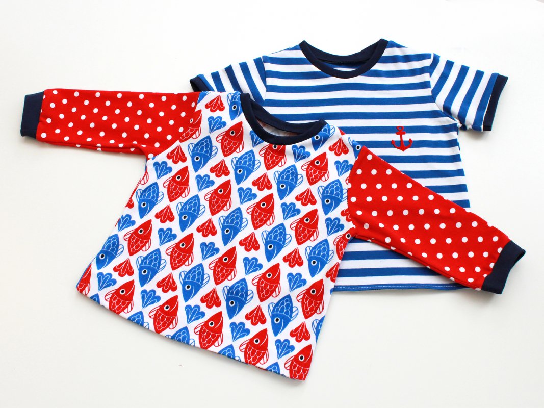 Zwei Kinder-Shirts: eines mit rot-blauem Fischmuster und gepunkteten Ärmeln, das andere blau-weiß gestreift mit kleinem roten Anker