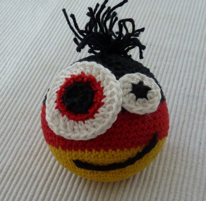 Gehäkelte Amigurumi-Kugel mit zwei großen Augen, schwarzer Quaste und gesticktem Mund