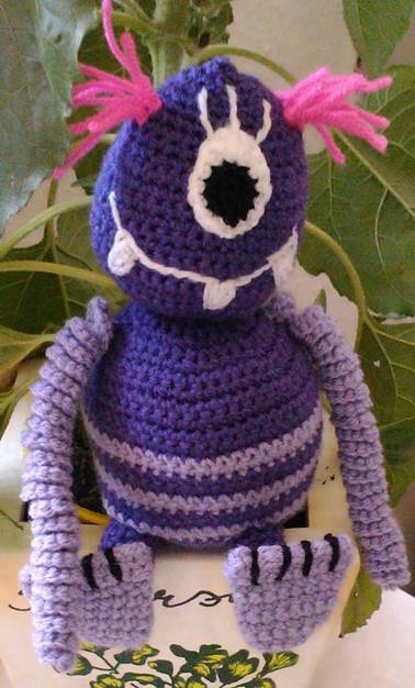 Lila gehäkeltes einäugiges Amigurumi
-Monster mit pinken Fransen