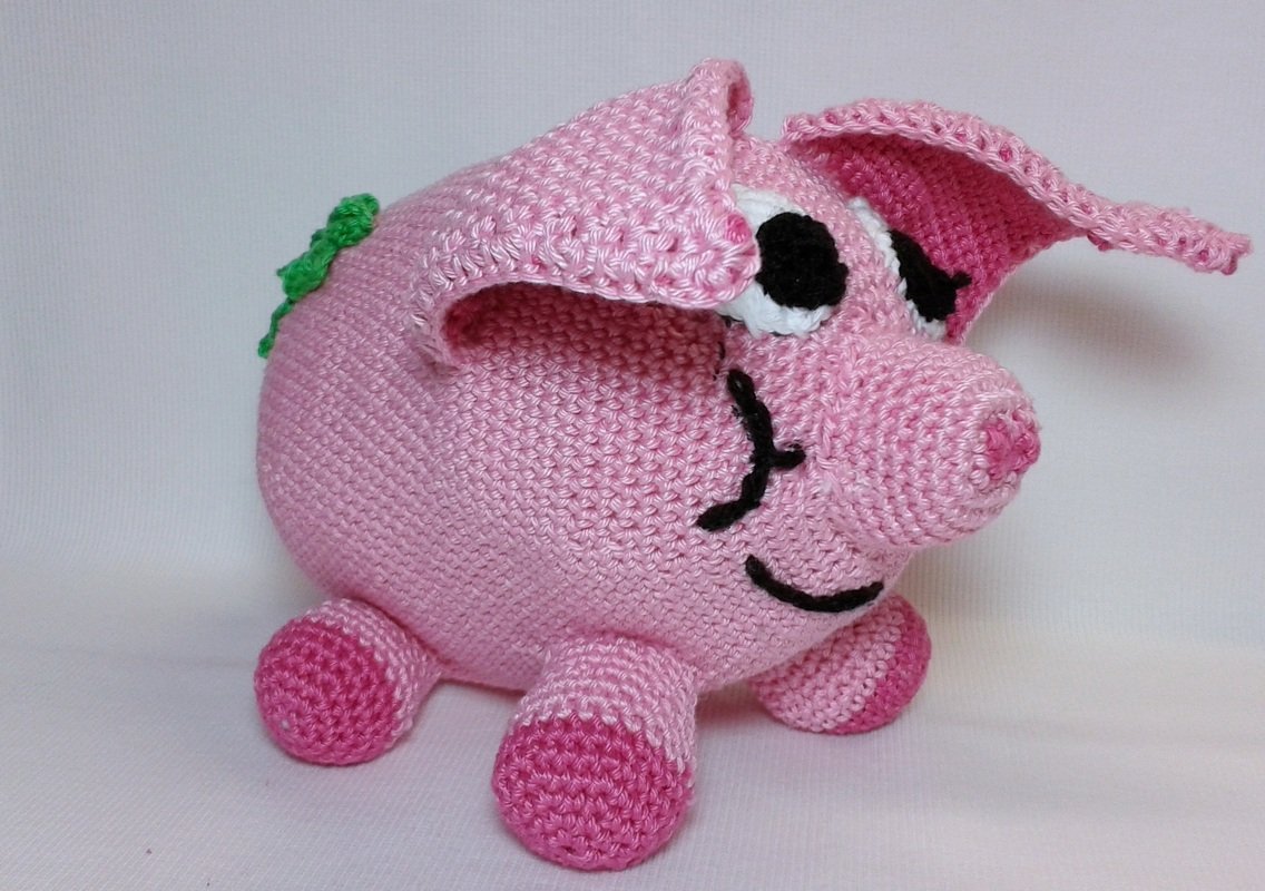 Rosa gehäkeltes Amigurumi-Glücksschwein mit Schlappohren, aufgesticktem Gesicht und grünem Kleeblatt
