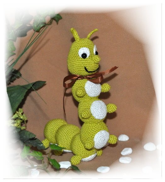 Grüne gehäkelte Amigurumi-Raupe mit weißen Bauchflecken und brauner Schleife