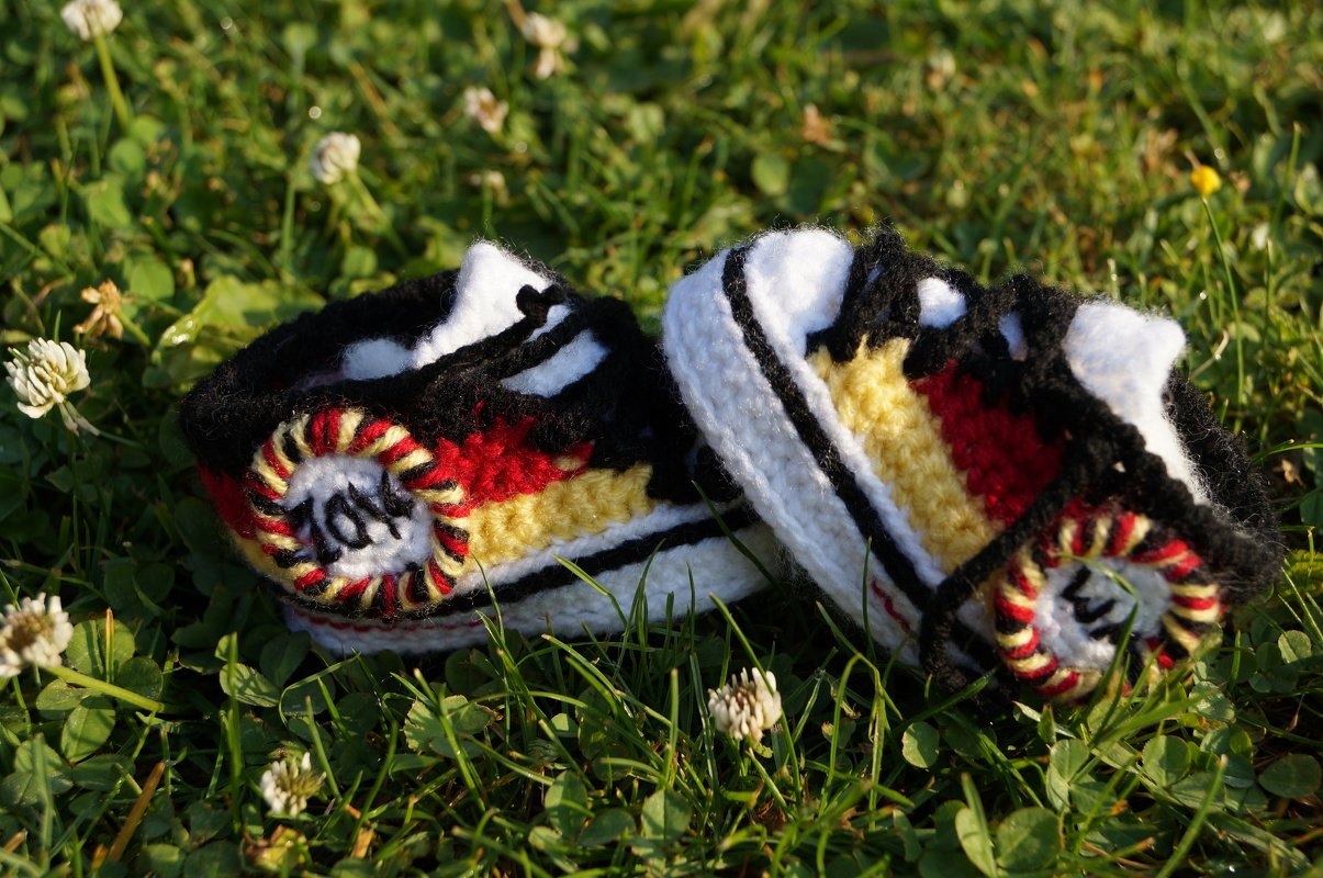 Nahaufnahme von zwei DIY‑gehäkelten Babyschuhen im Sneaker‑Design mit farbigen Streifen auf Gras