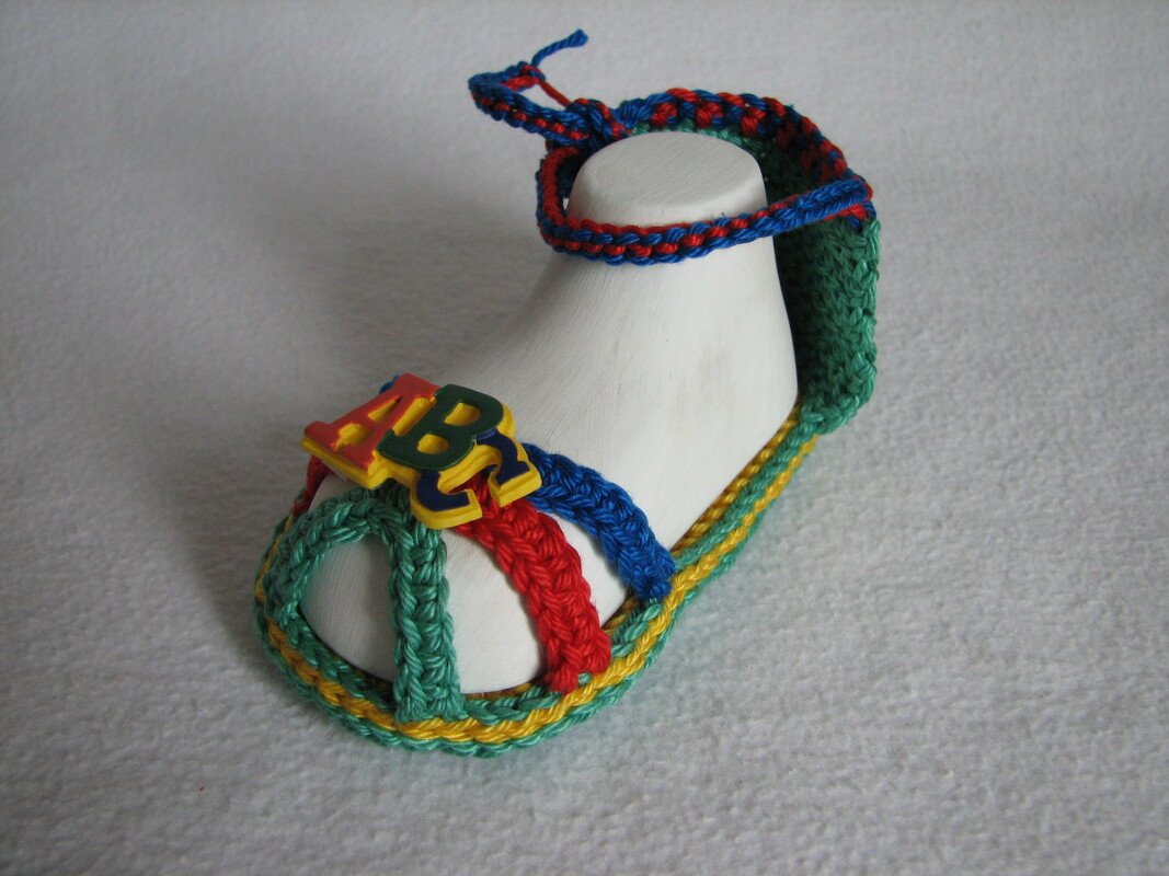 Gehäkelte Babysandale in Grün, Blau, Rot und Gelb mit ABC-Buchstaben auf weißer Schuhform