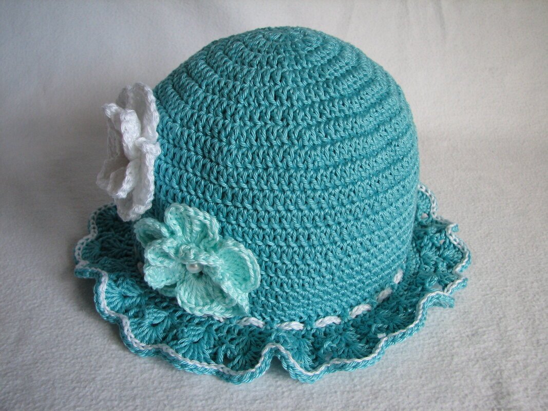 Gehäkelte türkise Babymütze mit weißen und hellblauen Blumen und gewelltem Rand