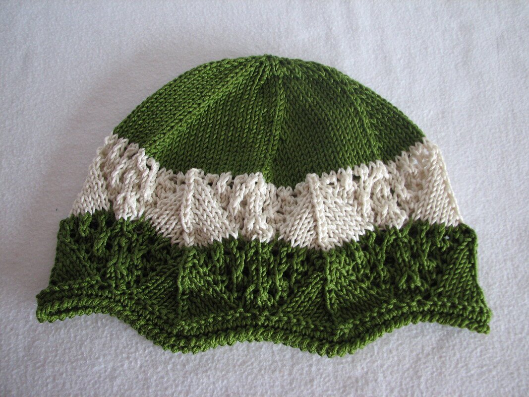 Grün-weiße gestrickte Babymütze mit Struktur- und Lochmuster und gewelltem Rand auf hellem Untergrund