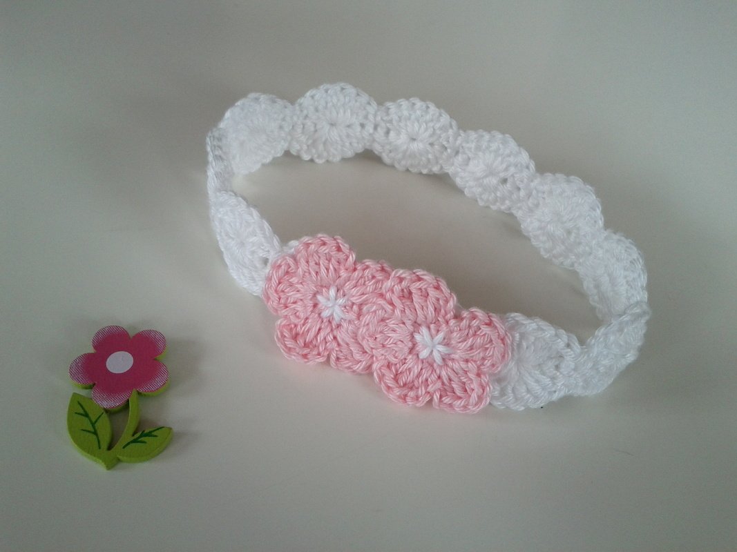 Weißes gehäkeltes Baby-Stirnband mit drei rosa Blüten und weißen Blütenmitten