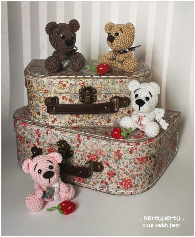 Vier gehäkelte Amigurumi-Teddybären (braun, beige, weiß, rosa) auf gestapelten blumengemusterten Koffern, mit gehäkelten Erdbeeren.