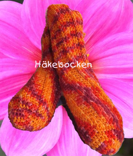 Zwei gehäkelte Socken in Orange- und Rottönen auf einer großen pinken Blüte