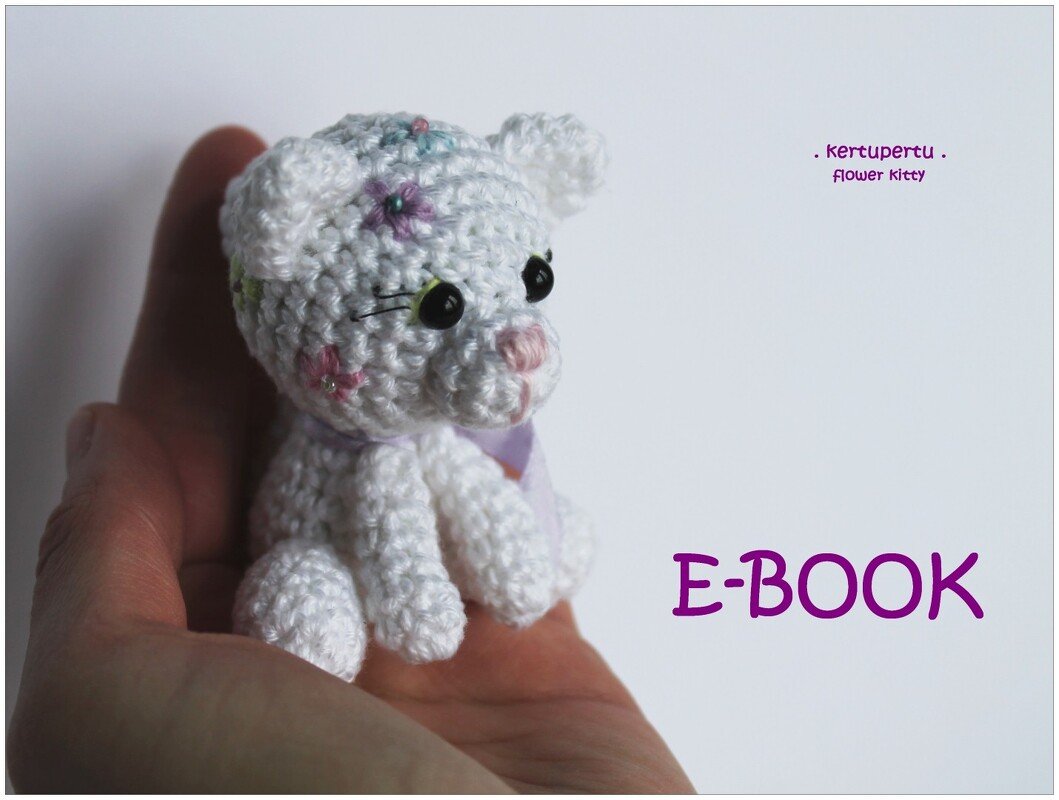 Hand, die ein kleines weißes gehäkeltes Amigurumi-Kätzchen mit aufgestickten Blumen hält.