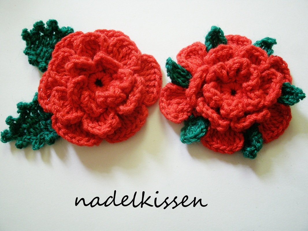 Zwei handgehäkelte rote Rosen mit grünen Blättern, Nahaufnahme