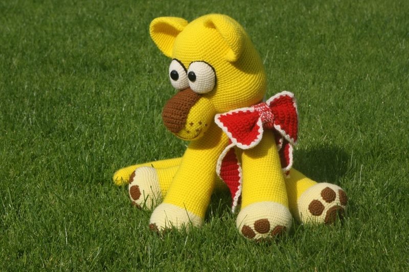 Gehäkelter gelber Amigurumi-Hund mit roter Schleife auf Gras