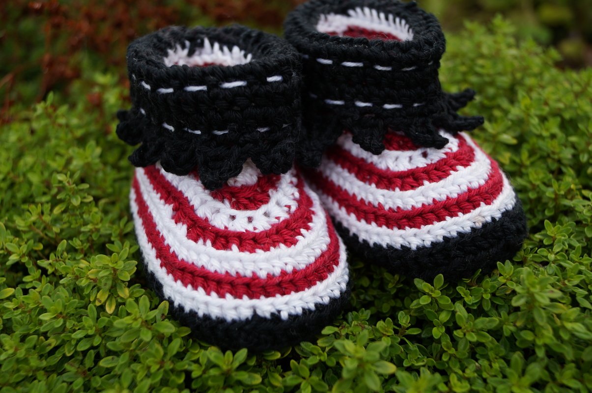 Gehäkelte Babyschuhe mit rot-weißen Streifen und schwarzer Rüsche, Nahaufnahme