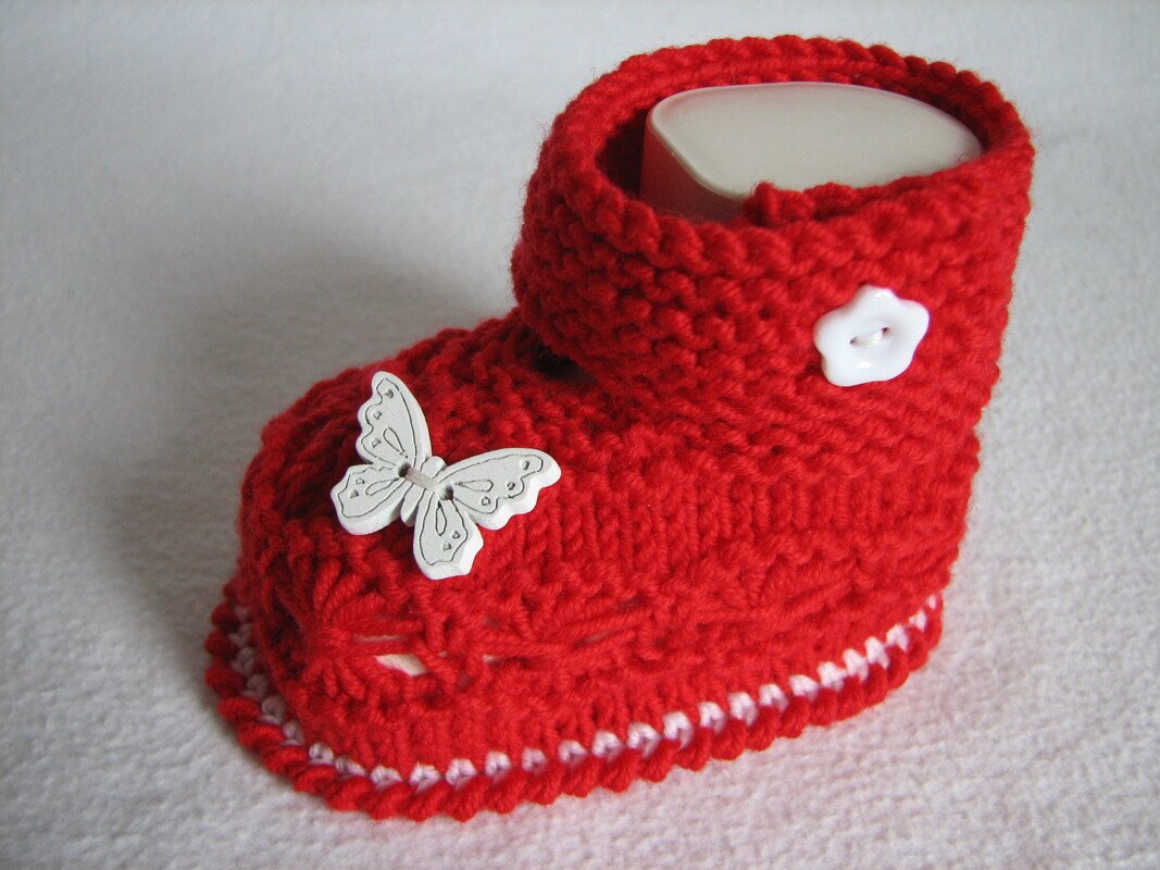 Roter handgestrickter Babyschuh mit weißer Schmetterlingsapplikation und Blütenknopf