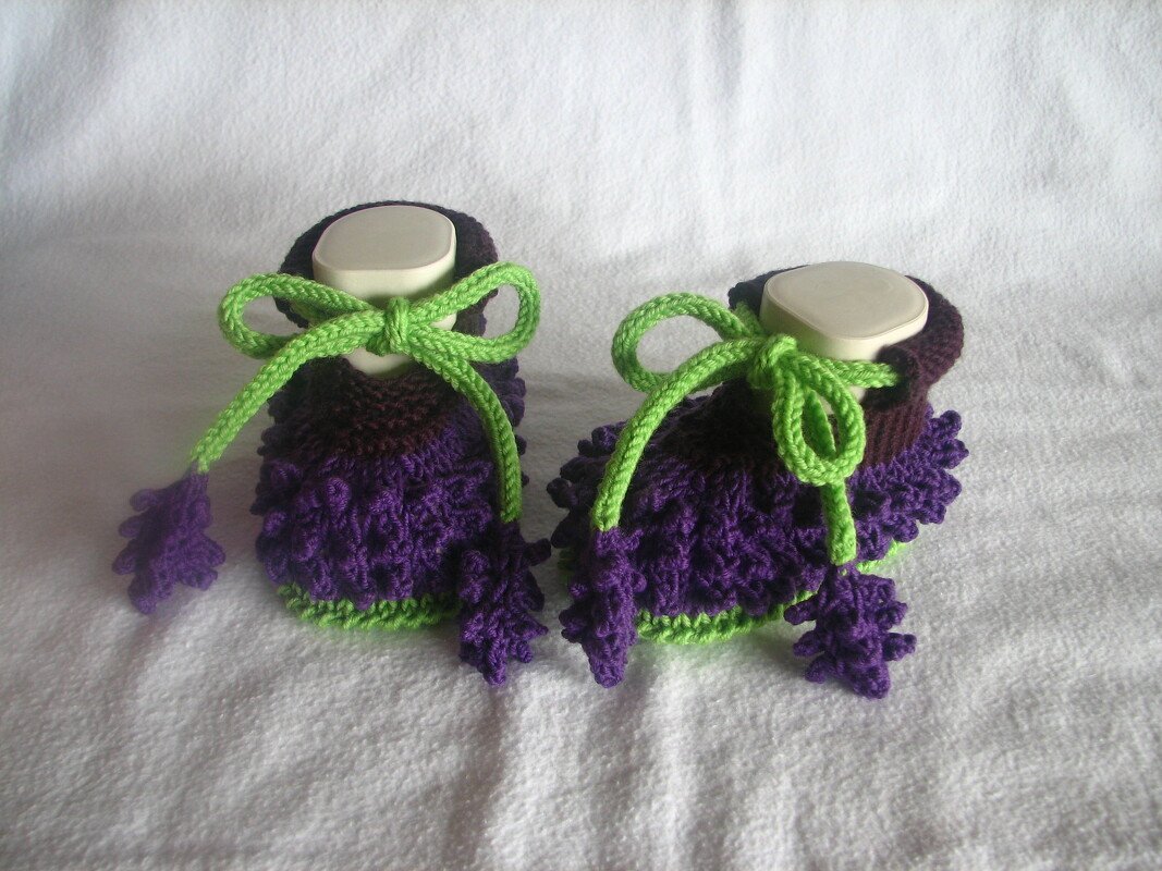 Detailaufnahme gestrickter lila Babyschuhe mit Rüschen und grüner Kordel