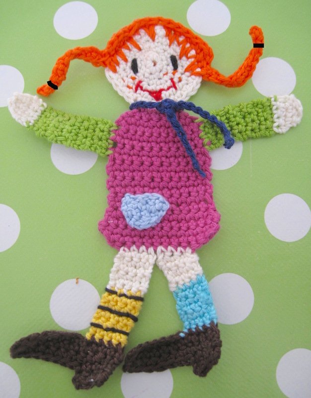Nahaufnahme einer gehäkelten Puppe mit pinkem Kleid, roten Zöpfen, bunten Socken und braunen Schuhen.