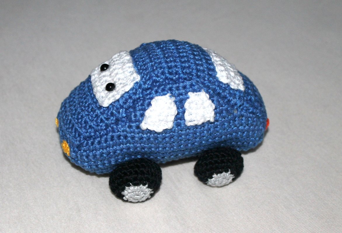 Gehäkeltes blaues Amigurumi-Auto mit weißen Fenstern und schwarzen Rädern