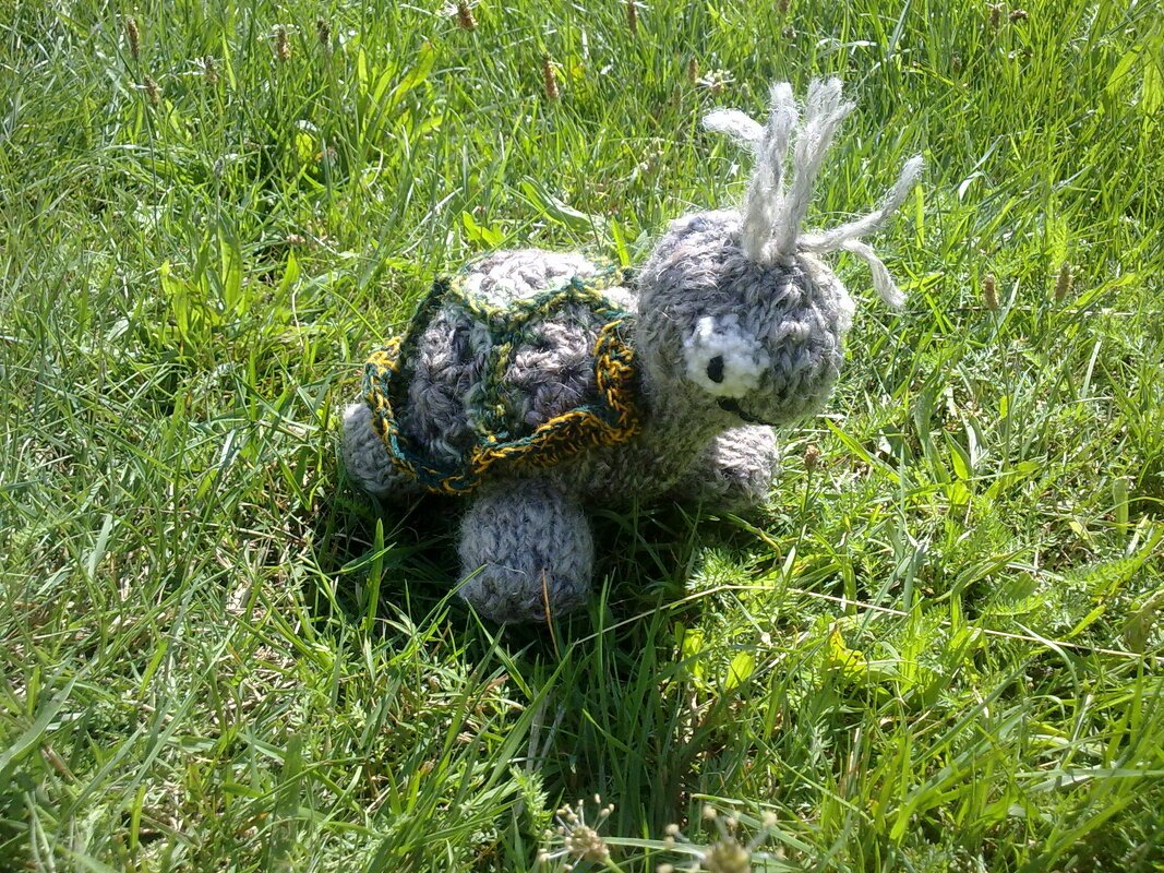 Kleine graue Amigurumi-Schildkröte mit grün-gelbem Panzer auf grünem Gras