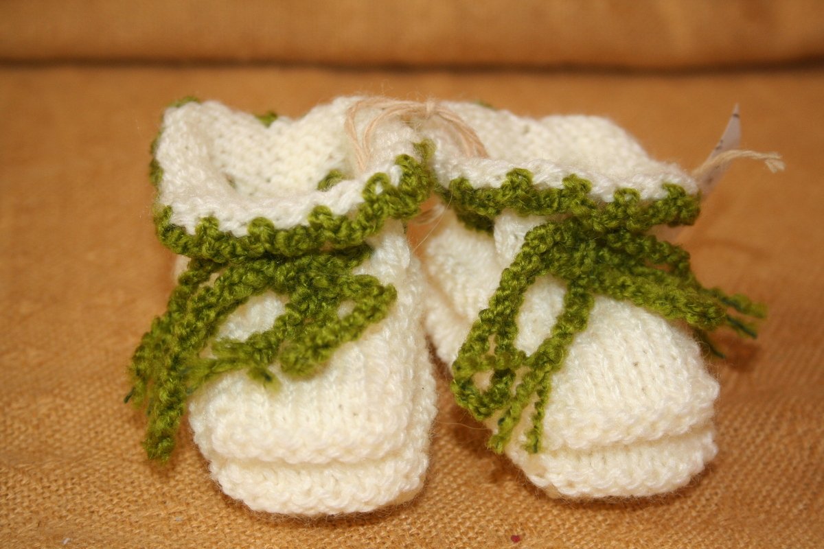 Kleine gestrickte Booties mit grünem Schnürband und Rüschenkante