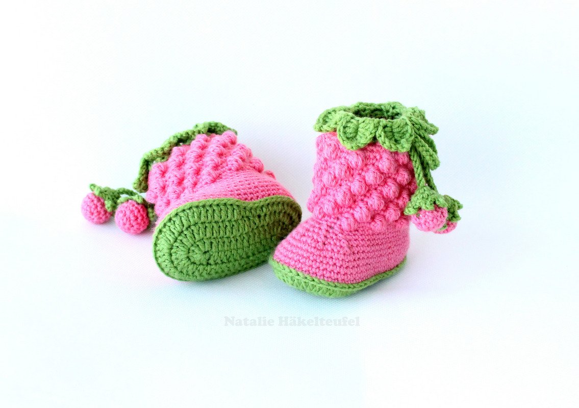 Pair of pink and green crocheted baby booties with a strawberry design, one upright and one on its side.
