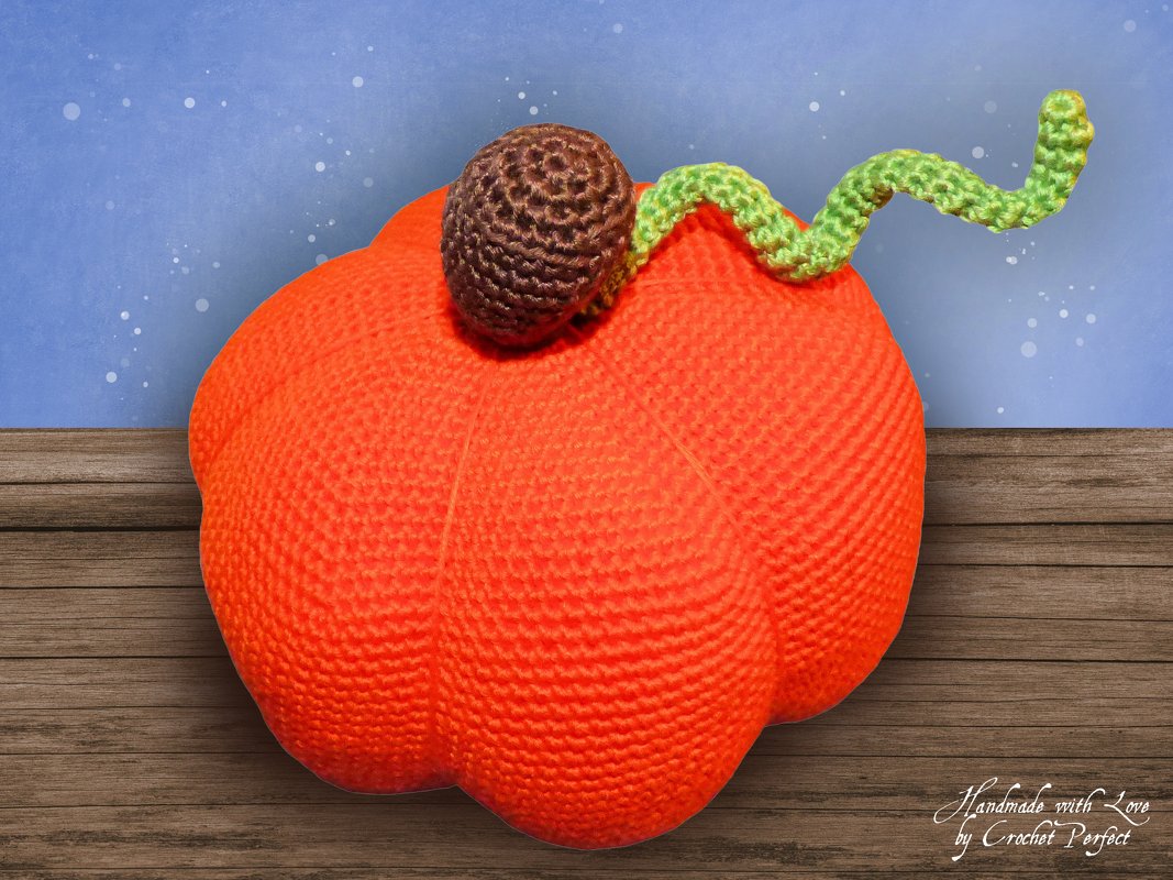 Gehäkelter oranger Kürbis mit braunem Stiel und grüner Ranke auf Holzuntergrund