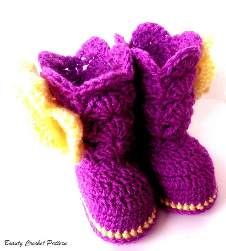 Zwei handgehäkelte Babyschuhe in Lila mit gelben Details auf weißem Hintergrund