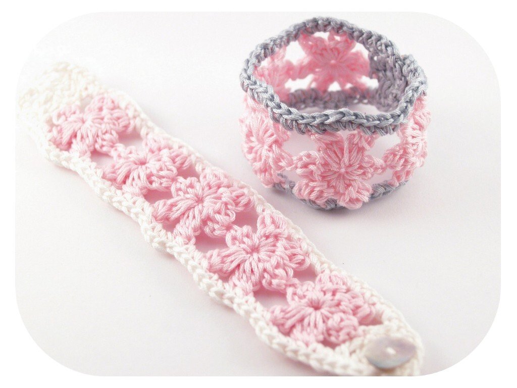 Handgehäkeltes rosa-weißes Armband mit Knopf und kleines rosa-graues Körbchen mit Blütenmuster auf hellem Hintergrund.