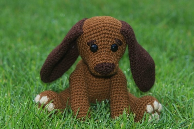 Gehäkeltes braunes Amigurumi-Hündchen mit langen Schlappohren sitzend im Gras