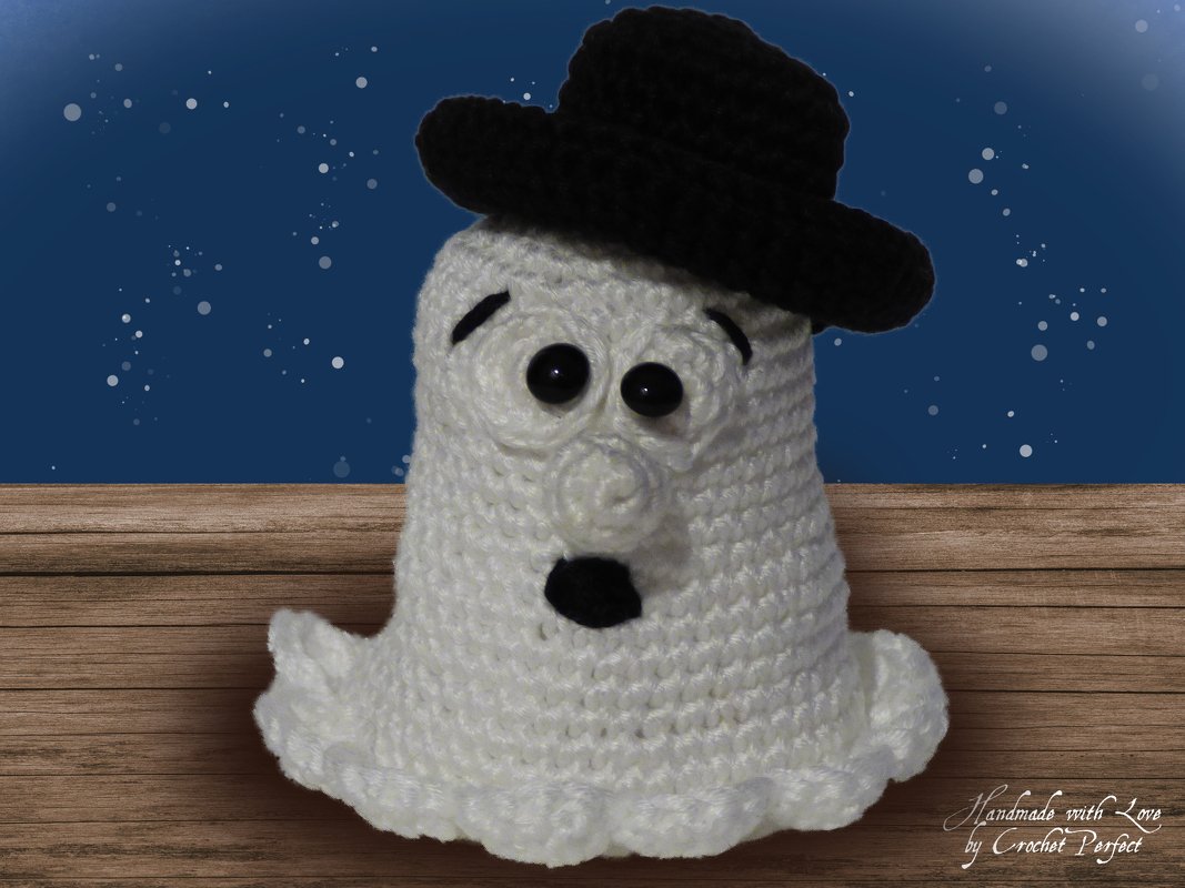 Weißer Häkelgeist mit gezacktem Saum und schwarzem Hut auf Holzbrett