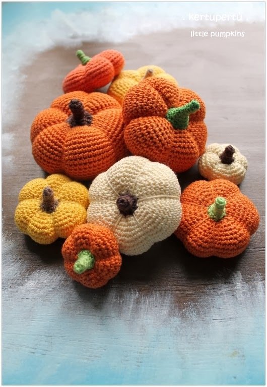 Mehrere handgehäkelte Mini-Kürbisse in Orange, Gelb und Creme auf Holztisch
