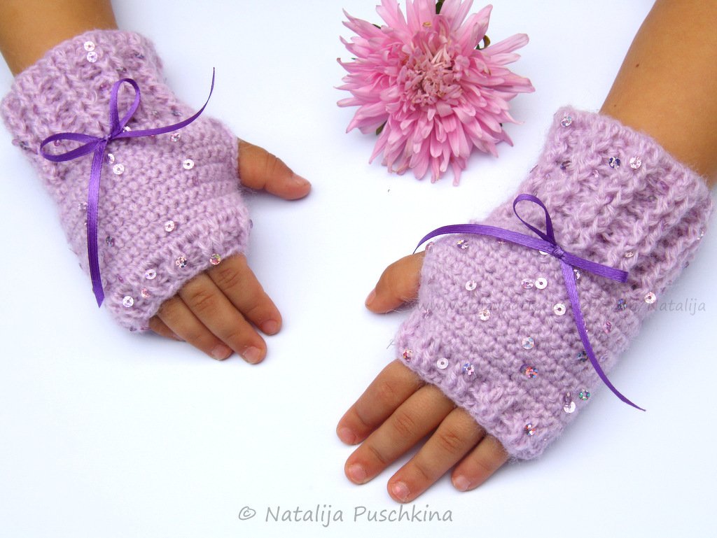 Kinderhände mit lila gehäkelten fingerlosen Stulpen, bestückt mit Pailletten und violettem Schleifenband