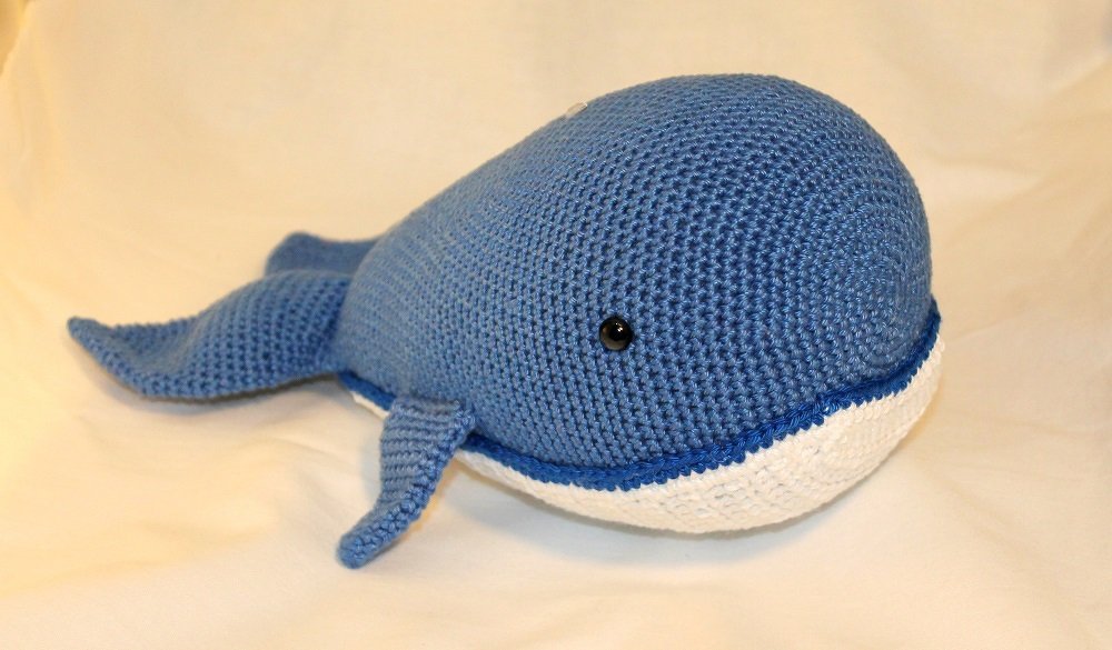 Gehäkelter blauer Amigurumi-Wal mit weißem Bauch und schwarzen Augen