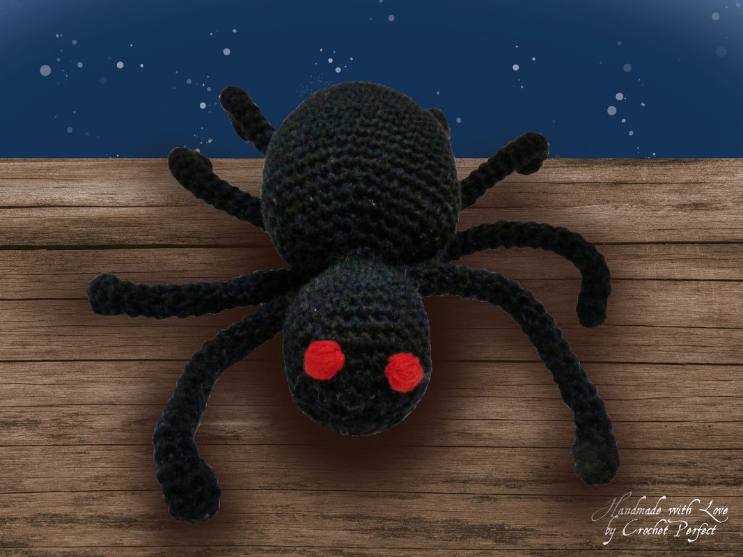 Schwarze gehäkelte Spinne mit roten Augen auf Holzplanken vor dunklem Himmel
