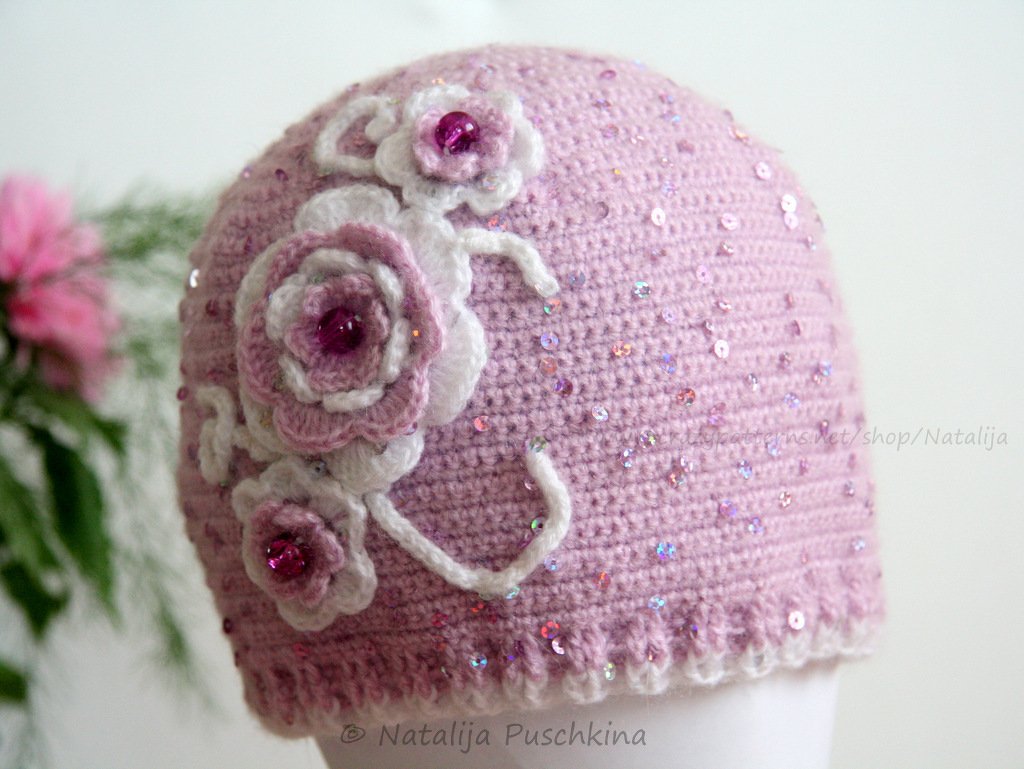 Rosafarbene gehäkelte Mütze mit weißen und rosa Blumenapplikationen und Pailletten