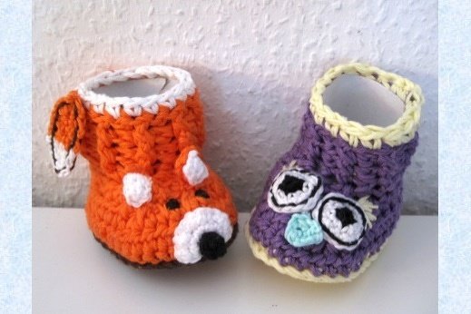 Zwei gehäkelte Babyschuhe, links orange mit Fuchsapplikation, rechts violett mit Eulenapplikation