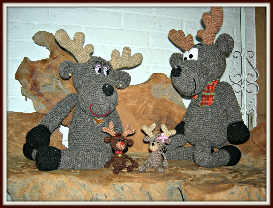 Zwei große graue gehäkelte Rentiere mit Geweihen und zwei kleine Amigurumi-Rentieranhänger auf Holzdeko