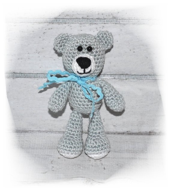 Gehäkelter grauer Amigurumi-Teddybär mit hellblauer Schleife auf hellem Holzuntergrund