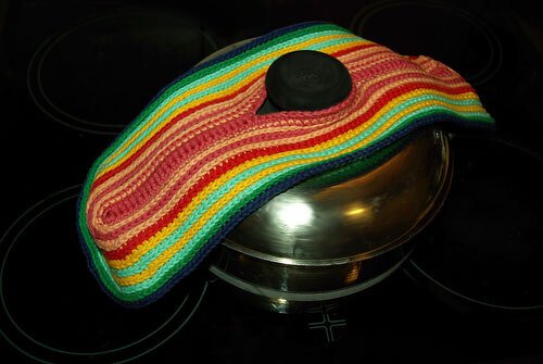 Gehäkelter Topfschoner in Regenbogenstreifen auf einem Metalltopf