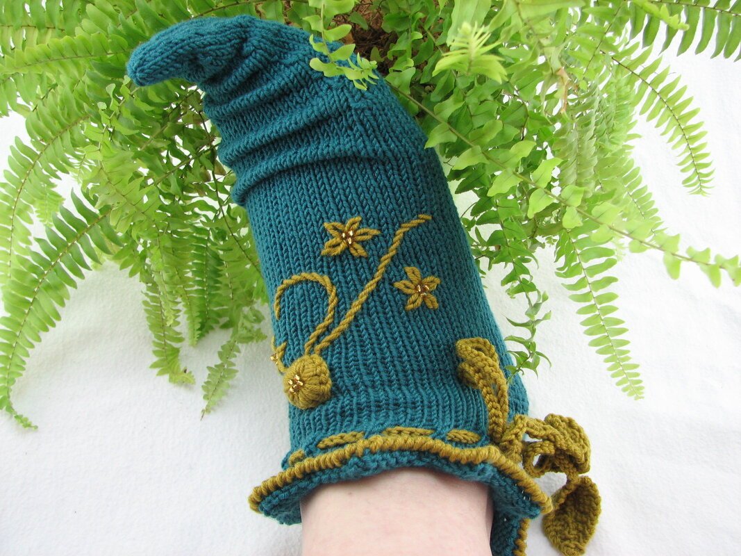 Türkisfarbene, gestrickte Zipfel‑Socke mit goldgelber Blumenstickerei und gerüschtem Bund