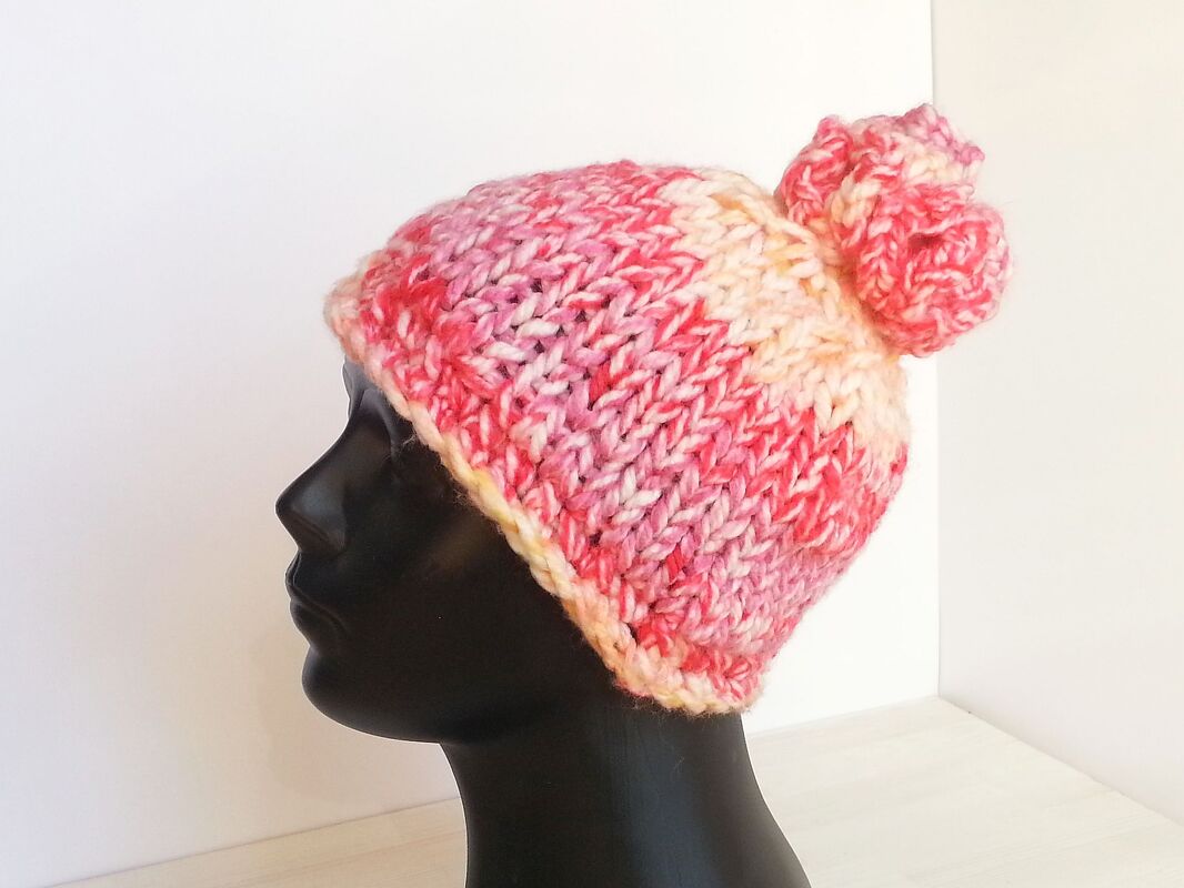 Rosa melierte Knooking-Mütze mit Bommel auf schwarzem Schaufensterkopf, Seitenansicht