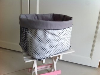 Viereckiger Stoffkorb mit schwarzen Punkten auf weißem Grund, schwarz-weißem Karomuster an den Seiten und grauem Innenfutter auf einem kleinen Hocker