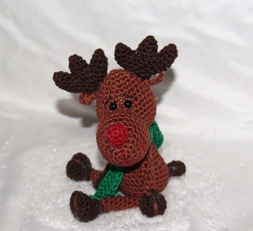 Gehäkeltes Amigurumi-Rentier in Braun mit roter Nase, dunkelbraunen Geweihen und grünem Schal, sitzend