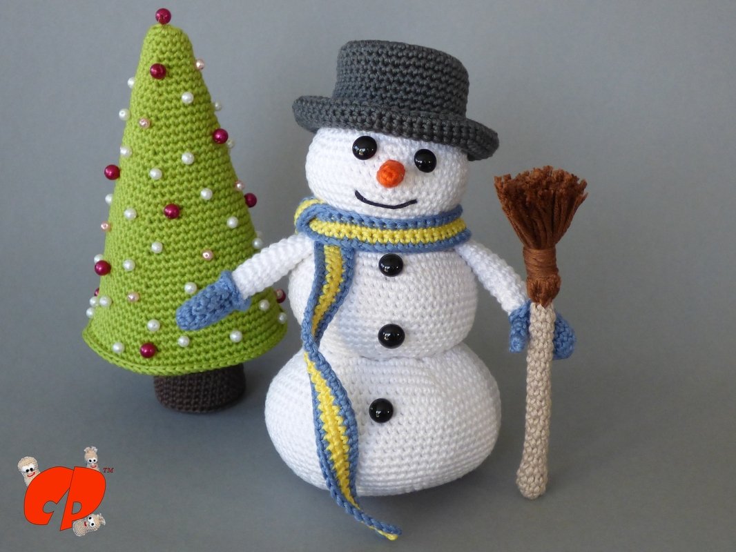 Gehäkelter Schneemann mit grauem Zylinder, blau-gelbem Schal und Besen neben grünem Weihnachtsbaum mit Perlen