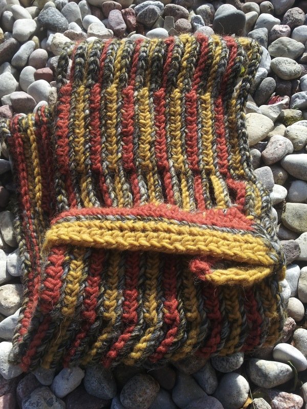 Folded striped crocheted cowl in mustard, rust and charcoal gray on pebbles