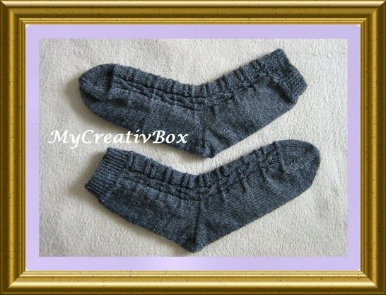 Paar grauer handgestrickter Socken mit Rippenbündchen und Zopfmuster auf hellem Untergrund