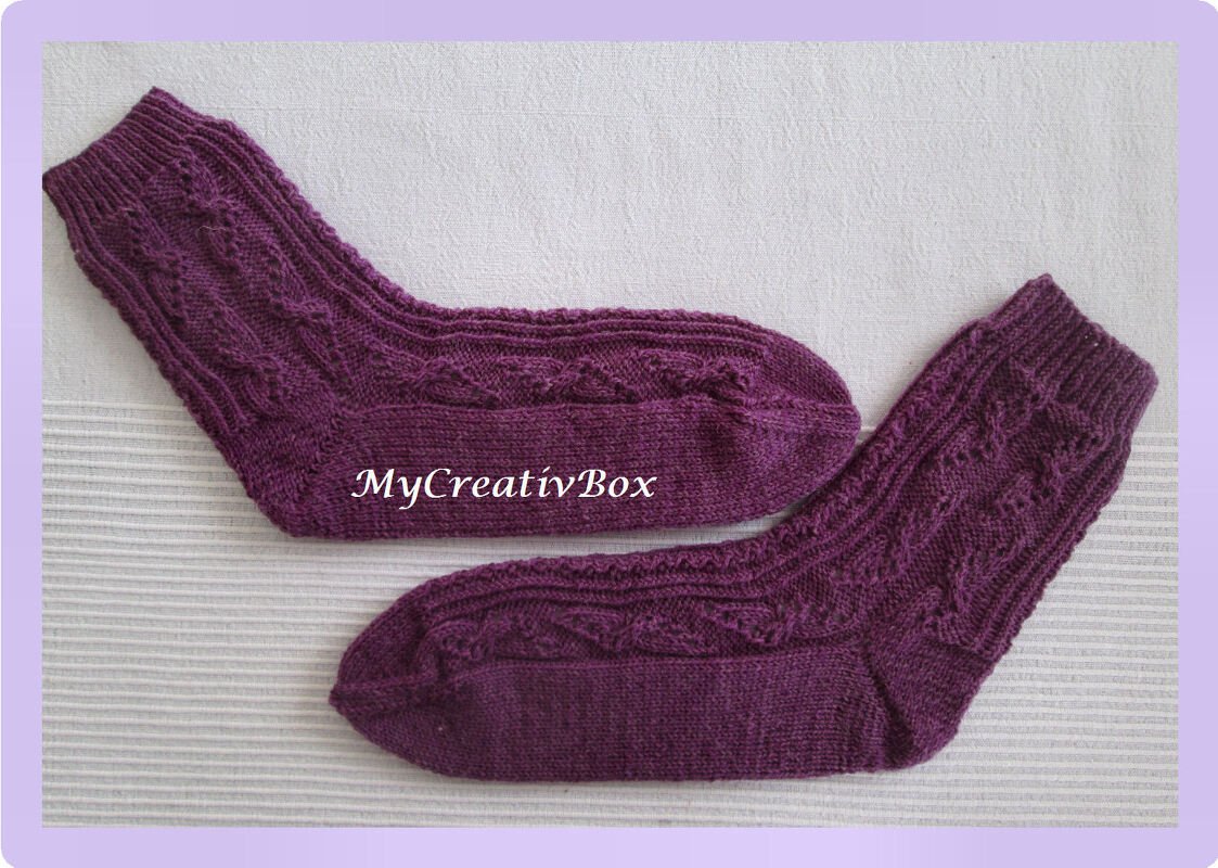 Paar violetter, gestrickter Socken mit Zopfmuster auf hellem Stoff
